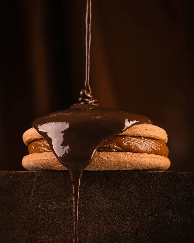 Un hilo de chocolate derretido baña la tapa de un alfajor Malfatti y chorrea por el costado hasta la tabla.