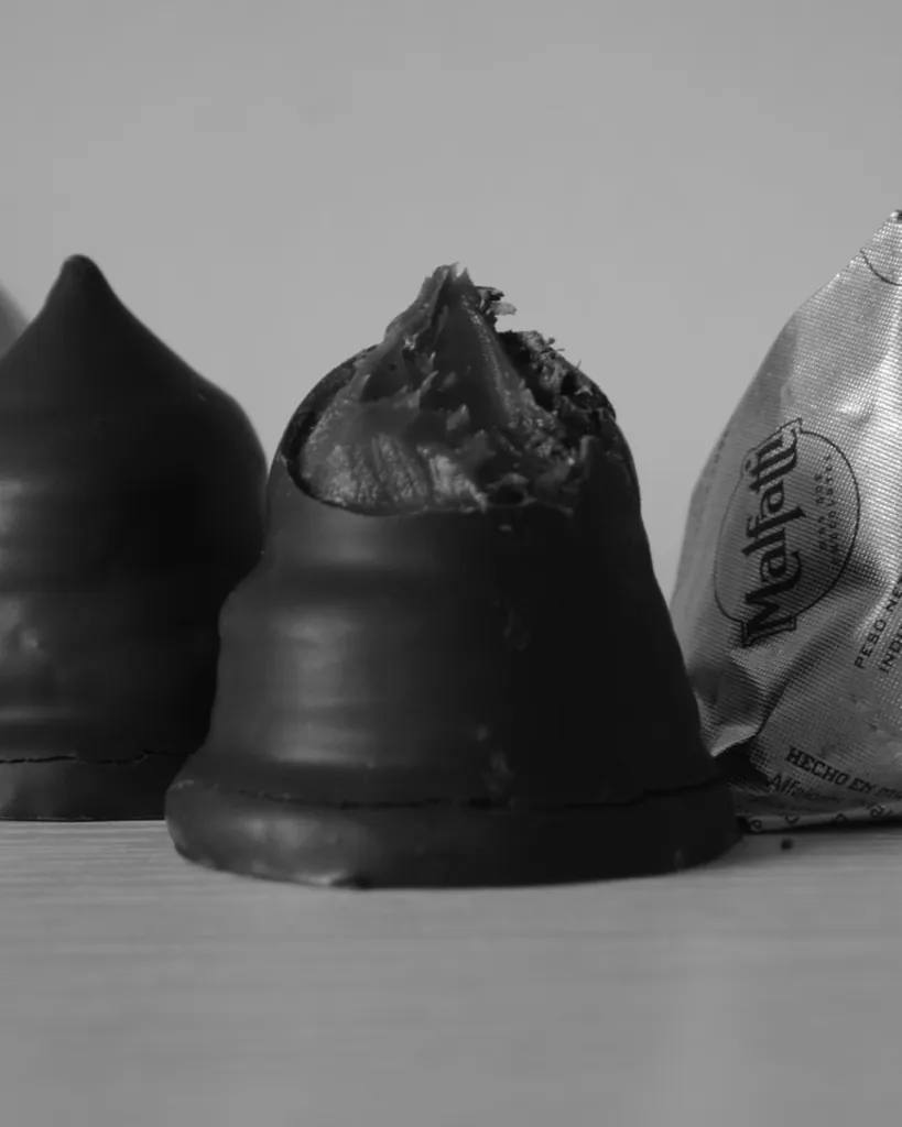 Conottes Malfatti en blanco y negro: uno de chocolate, mordido, entre otros envueltos en papel plateado.