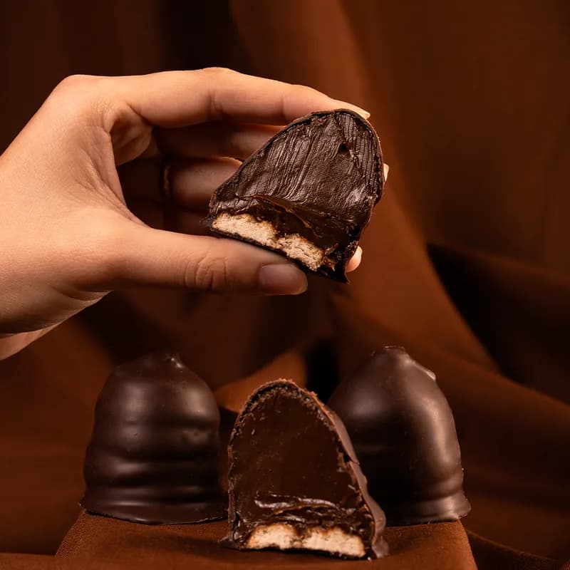 Conottes Malfatti bañados en chocolate; uno cortado deja ver el dulce de leche sobre la base de galleta.
