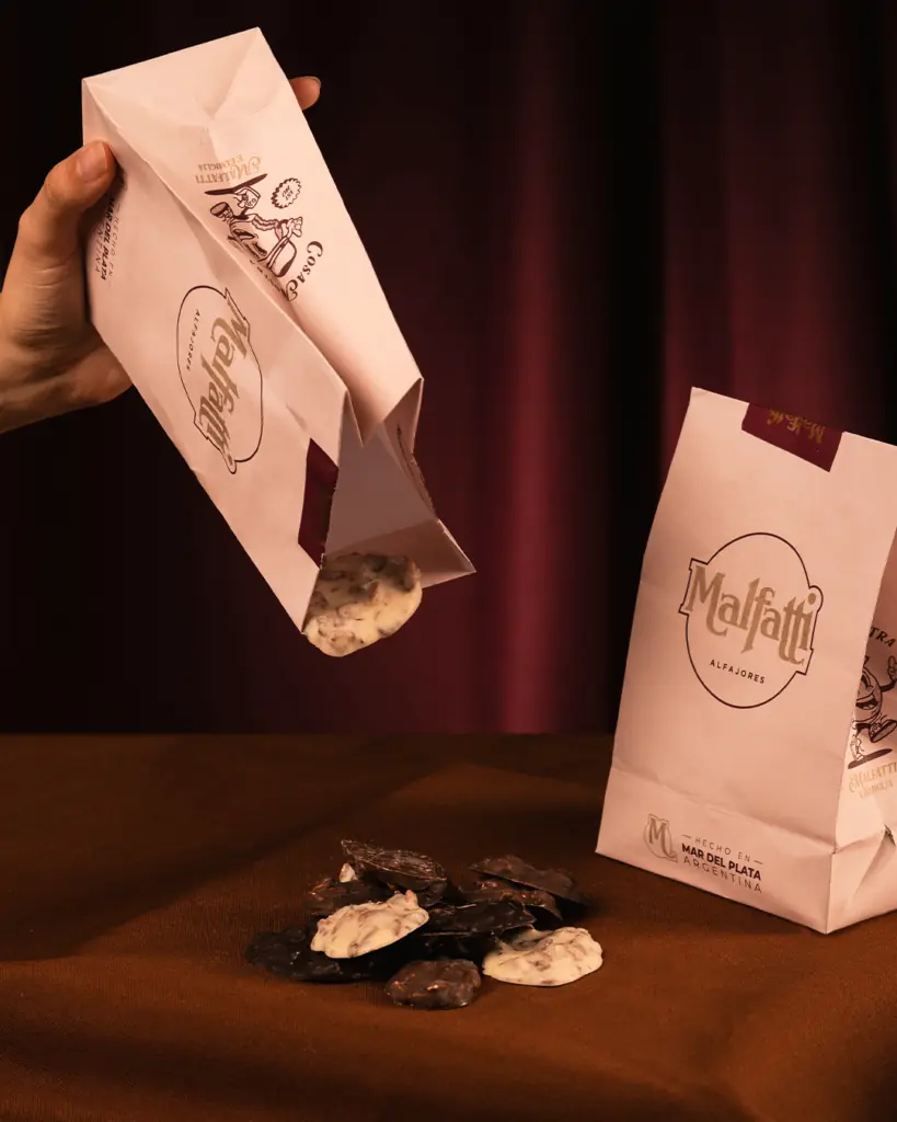 Bolsas de papel con el logo Malfatti; de una caen chocolates artesanales bañados.